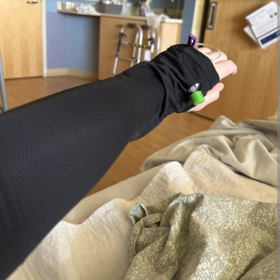 Person wearing black adaptive port access sleeve with medical tubing in a hospital or recovery setting